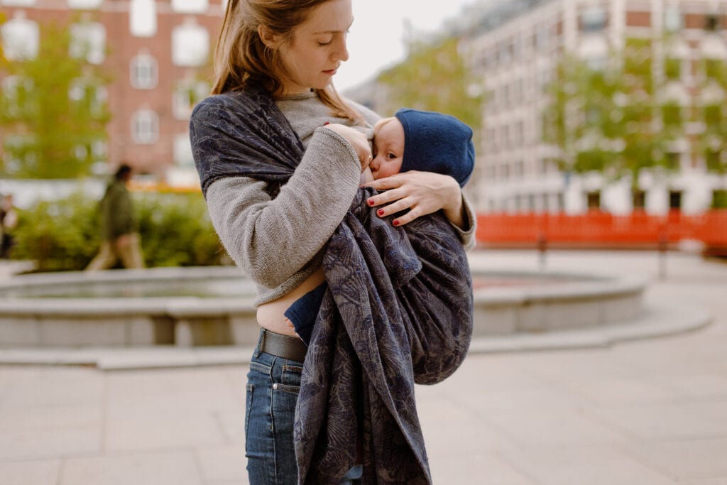 A mother breastfeeding her toddler while he is carried by her in Morpho by Levate wraps.